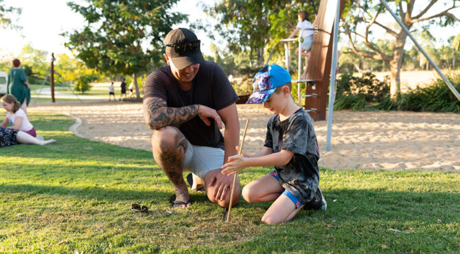 father and son using a stick to make a fire in north rockhampton