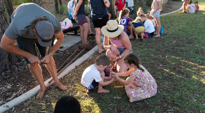 mother kneeling down beside two children learning how to build a fire in parkhurst