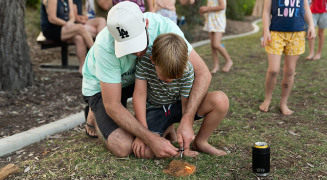 father and son sitting on the grass learning how to start a fire using a flint in rockhampton