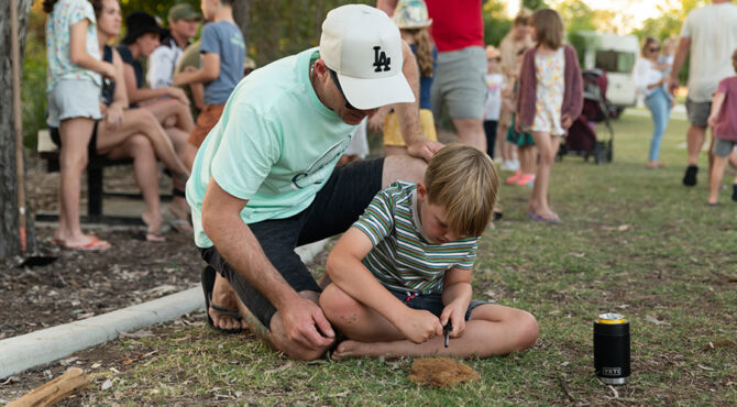 father and son sitting on the grass learning how to start a fire using a flint in rockhampton