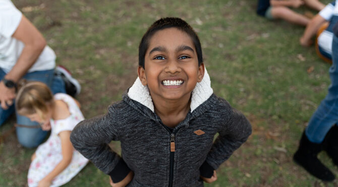 young indian boy in grey jacket with hands in his pockets looking up and smiling at community event at edenbrook estate in rockhampton queensland