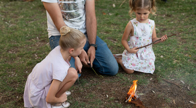 two girls sitting with their dad learning how to make fire traditionally in Rockhampton