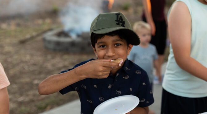 young indian boy with green hat smiling and eating a smore in rockhampton at community event